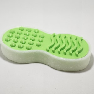 Puede incluir: Una esponja de baño verde con una superficie texturizada en un lado y una superficie ondulada en el otro.
