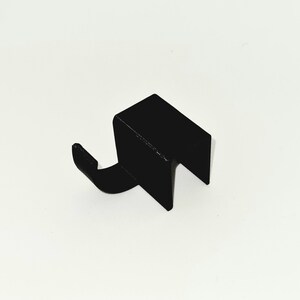 May include: A black metal hook with a rectangular body and a curved hook extending from one side. The hook is designed to hang items and is likely made of durable metal.