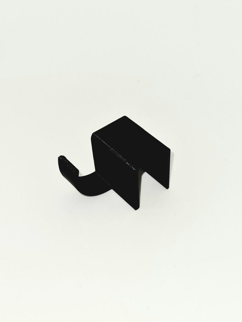 May include: A black metal hook with a rectangular body and a curved hook extending from one side. The hook is designed to hang items and is likely made of durable metal.