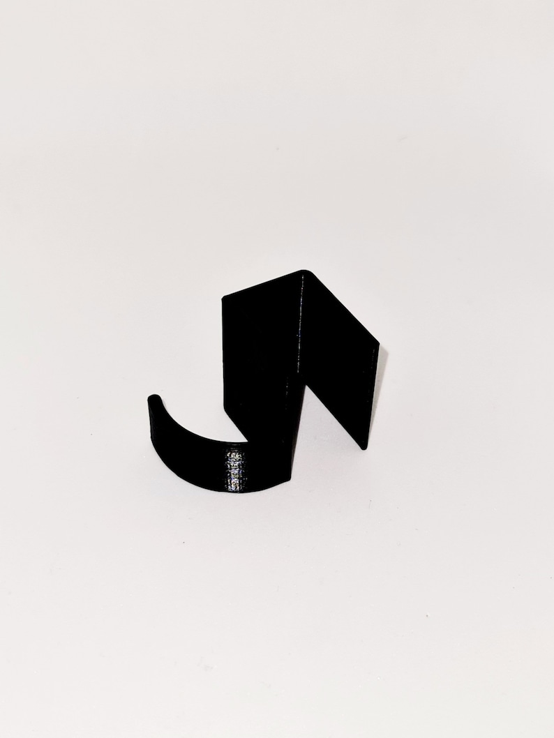 May include: A black, abstract hook-shaped object. The hook has a curved lower section and a right-angled upper section. The object is set against a plain white background, highlighting its form and design.