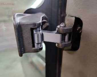 May include: A close-up of a silver metal hinge attached to a black metal door frame. The hinge has a silver metal pin and a black metal arm.
