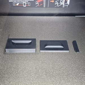 May include: Three 3D printed black plastic pieces, two rectangular with a recessed handle shape and one smaller rectangular piece.