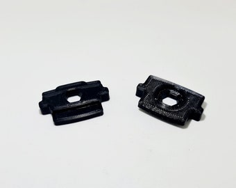 May include: Two black plastic pieces with a hexagonal hole in the center. The pieces have a textured surface and are designed to be used as a connector or fastener.