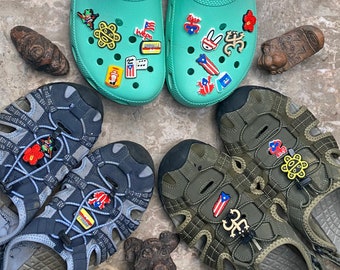 May include: Four pairs of sandals with colorful charms. The sandals are in various colors, including green, blue, brown, and black. The charms are in the shape of flags, animals, and other designs.