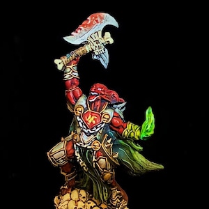 May include: A miniature fantasy figure of a red-skinned warrior, wielding a large axe with a bone-like handle and a blood-stained blade. The figure is adorned with armor and a green cape, standing atop a pile of skulls. A green energy effect emanates from the warrior's hand.