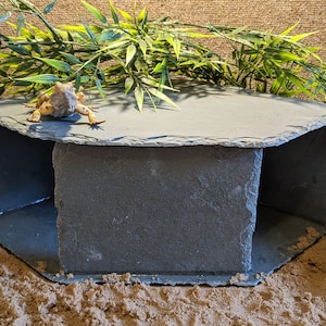 May include: A hexagonal slate hide with a small lizard on top. The hide is made of natural slate and has a rough texture. It is designed to provide a safe and secure hiding place for reptiles.