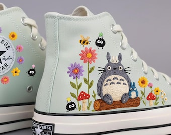 May include: Light green high-top sneakers with embroidered floral and cartoon character designs. The sneakers feature the Converse All Star logo on the side and a black and white sole.