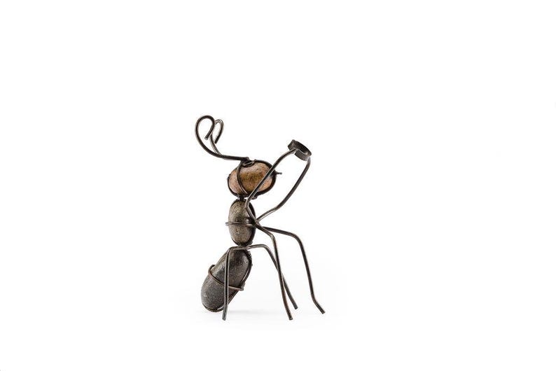 May include: A handcrafted metal ant sculpture with a unique design. The ant's body is formed from smooth, rounded stones, while its legs and antennae are made of dark metal wire. The sculpture is set against a plain white background.
