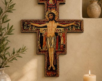 May include: A wall-mounted wooden cross featuring a central depiction of a figure with arms outstretched, surrounded by smaller figures in red, gold, and black tones. The cross has a decorative border and includes text near the top center.