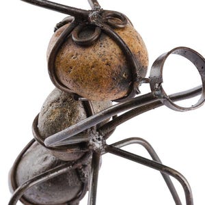 May include: A metal sculpture of an ant with a magnifying glass. The ant's body is made of stones and wire, with a magnifying glass held in its front legs. The sculpture is a unique piece of art.