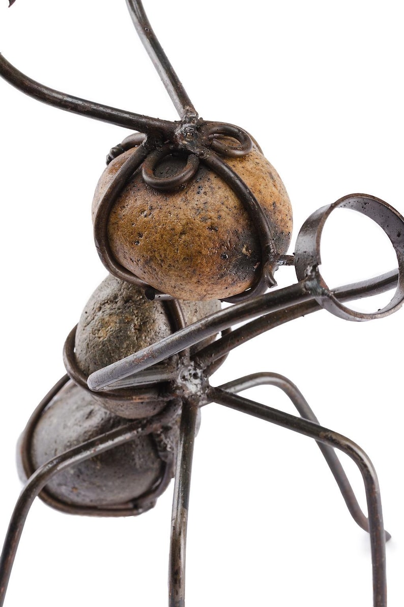 May include: A metal sculpture of an ant with a magnifying glass. The ant's body is made of stones and wire, with a magnifying glass held in its front legs. The sculpture is a unique piece of art.