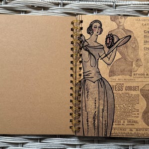May include: A brown notebook with a spiral binding. The cover features a vintage illustration of a woman in a dress and hat, with text from an old catalog. The text includes "Illustrated Catalog" and "Leo".