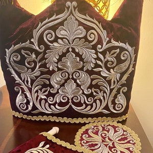 May include: A set of three burgundy velvet cushions with gold embroidered floral patterns. The cushions are decorated with a gold trim.