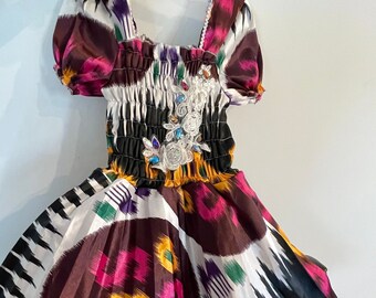 May include: A white, black, pink, yellow, and green patterned dress with a white lace and rhinestone embellishment on the bodice.