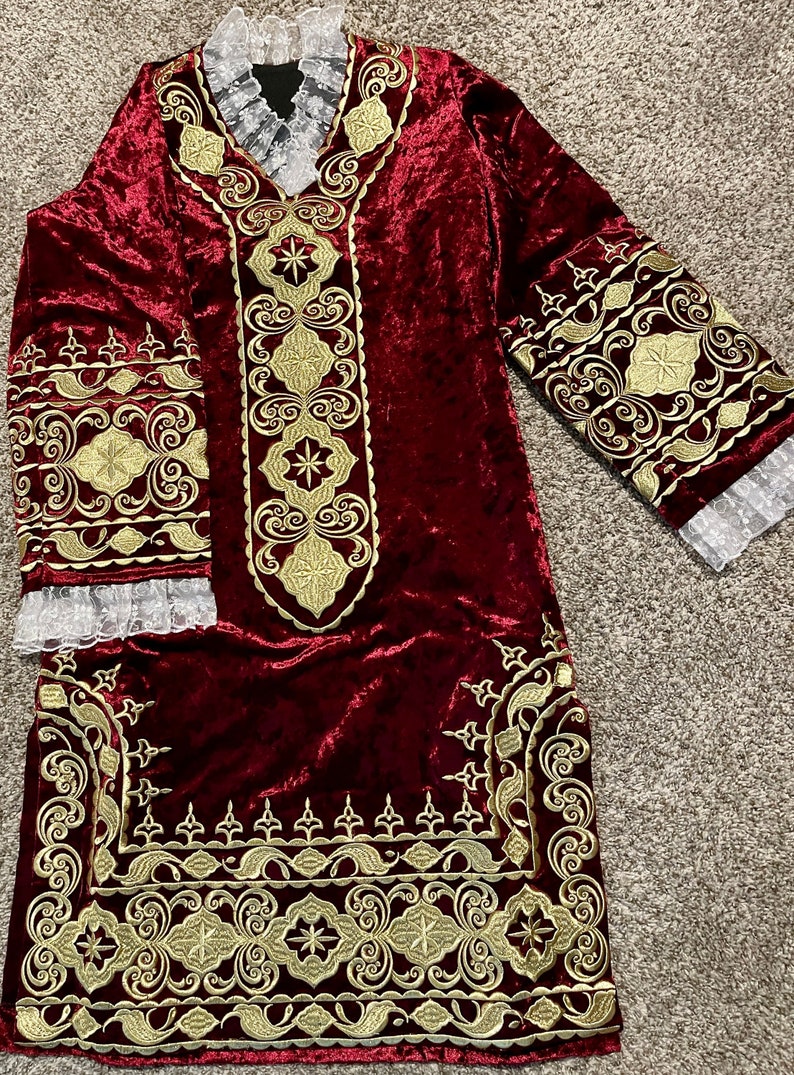 May include: A long, burgundy velvet robe with gold embroidery. The robe has a V-neckline and long sleeves with lace trim. The embroidery features intricate floral and geometric patterns.