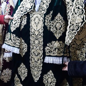 May include: A dark green velvet garment with intricate gold embroidery. The garment features a floral design and a lace trim.