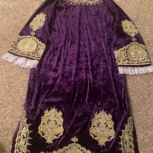 May include: A long, purple velvet robe with gold embroidery. The robe has a high neckline and long sleeves. The embroidery is intricate and features floral designs.