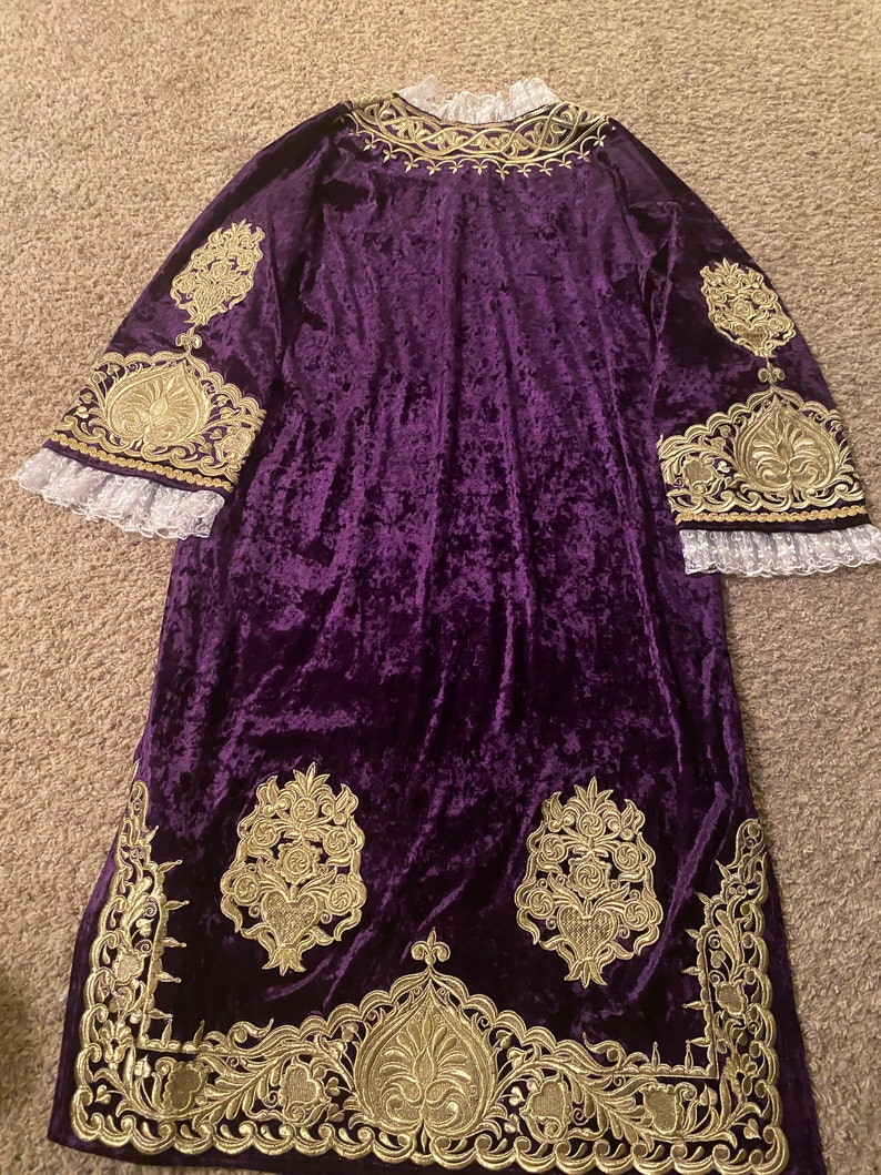 May include: A long, purple velvet robe with gold embroidery. The robe has a high neckline and long sleeves. The embroidery is intricate and features floral designs.