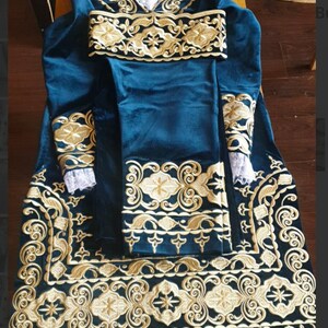 May include: A teal velvet robe with gold embroidery. The robe has long sleeves and a collar. The embroidery is intricate and features floral designs.
