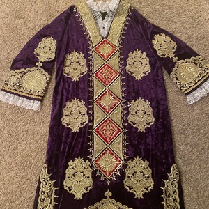 May include: A long, purple velvet robe with gold embroidery and red accents. The robe has a wide, V-neck collar and long sleeves with lace trim.