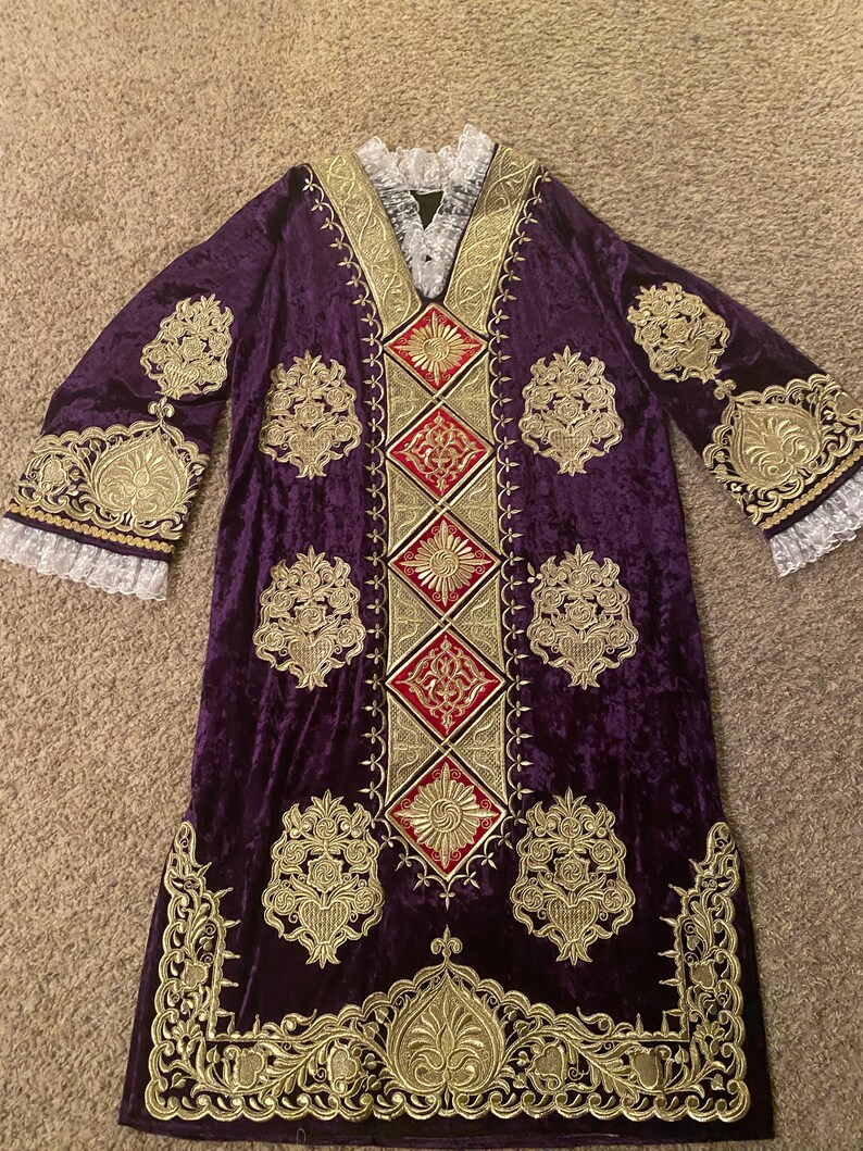 May include: A long, purple velvet robe with gold embroidery and red accents. The robe has a wide, V-neck collar and long sleeves with lace trim.