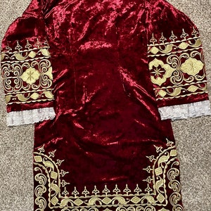 May include: A long-sleeved, burgundy velvet robe with gold embroidery around the cuffs and hem. The embroidery features intricate floral and geometric patterns.