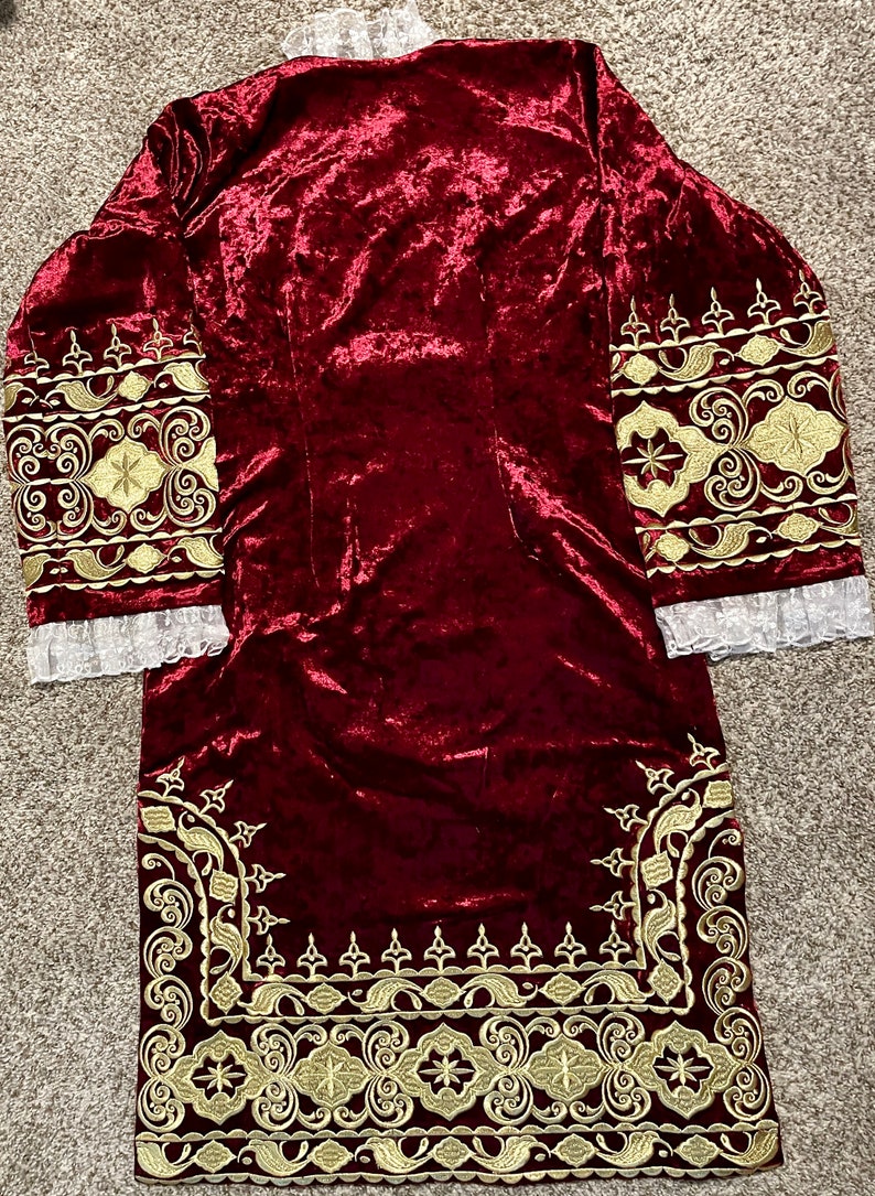 May include: A long-sleeved, burgundy velvet robe with gold embroidery around the cuffs and hem. The embroidery features intricate floral and geometric patterns.
