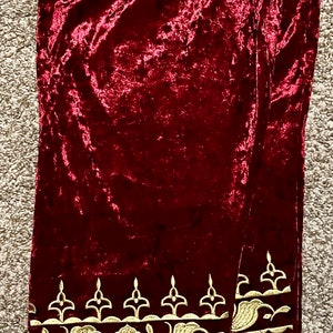 May include: A pair of burgundy velvet pants with gold embroidered trim. The trim features a repeating pattern of stylized flowers and leaves.