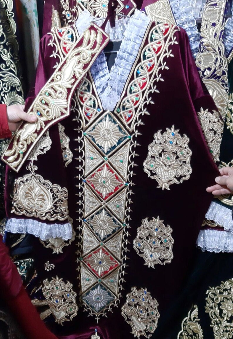 May include: A burgundy velvet robe with intricate gold embroidery and embellishments. The robe features a high collar and long sleeves with a decorative trim. The embroidery includes floral and geometric patterns.