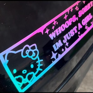 May include: A pink and blue gradient sticker with a cartoon Hello Kitty character and the text "WHOOPS, SORRY I'M JUST A GIRL" with stars around the text.