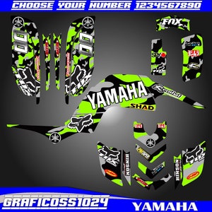 May include: Green, black, and gray camouflage graphic kit for a Yamaha ATV. The kit includes a large graphic with the word "YAMAHA" in white letters, as well as smaller graphics with logos for Fox Racing, GoPro, Bridgestone, and Yoshimura.