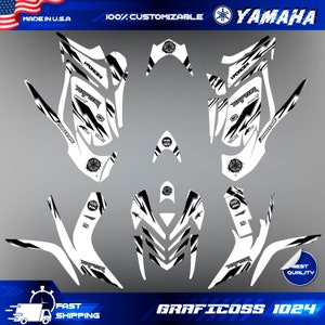 May include: Black and white graphic design kit for a Yamaha Raptor 700 ATV. The kit includes a variety of decals with the words "VForce4", "Raptor", "700", and "Bridgestone" printed on them.