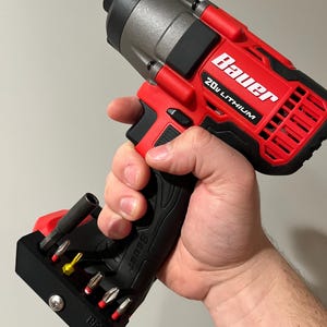 May include: A red and gray Bauer 20V Lithium impact driver with a black handle and a black bit holder. The bit holder contains various screwdriver bits. The tool is held in a hand.