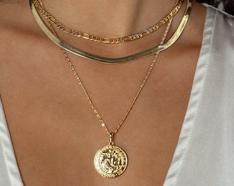 May include: A layered gold necklace set with a pendant featuring a round coin design. The pendant has a detailed design of a lion's head.