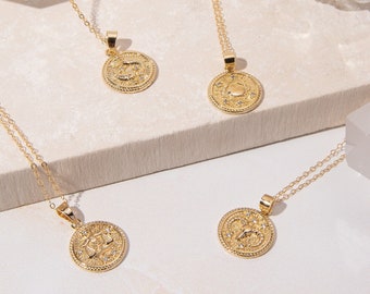 May include: Four gold necklaces with zodiac symbols on round pendants. The necklaces are displayed on a white surface with a white crystal and a glass bowl.