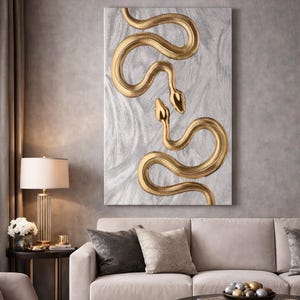 May include: A rectangular canvas art piece featuring two golden snakes on a textured, light gray background. The snakes are intricately detailed, with their bodies coiling and heads raised. The artwork is displayed in a living room setting.