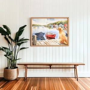 Puede incluir: Una pintura al agua enmarcada de un perro golden retriever sentado en un muelle de madera con vistas a un peque&ntilde;o puerto con barcos. La pintura est&aacute; colgada en una pared blanca con un banco de madera en primer plano.