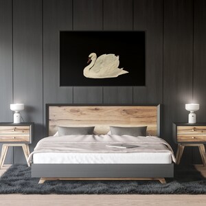 K&ouml;nnte beinhalten: Ein Schlafzimmer-Interieur mit einem Bett, zwei Nachttischen und Lampen. Das Bett hat ein h&ouml;lzernes Kopfteil und ein graues Fu&szlig;teil. Die Nachttische sind aus Holz und haben zwei Schubladen. Die Lampen sind wei&szlig; und haben ein schlichtes Design. Ein schwarz-wei&szlig;es gerahmtes Bild eines wei&szlig;en Schwans h&auml;ngt an der Wand &uuml;ber dem Bett.