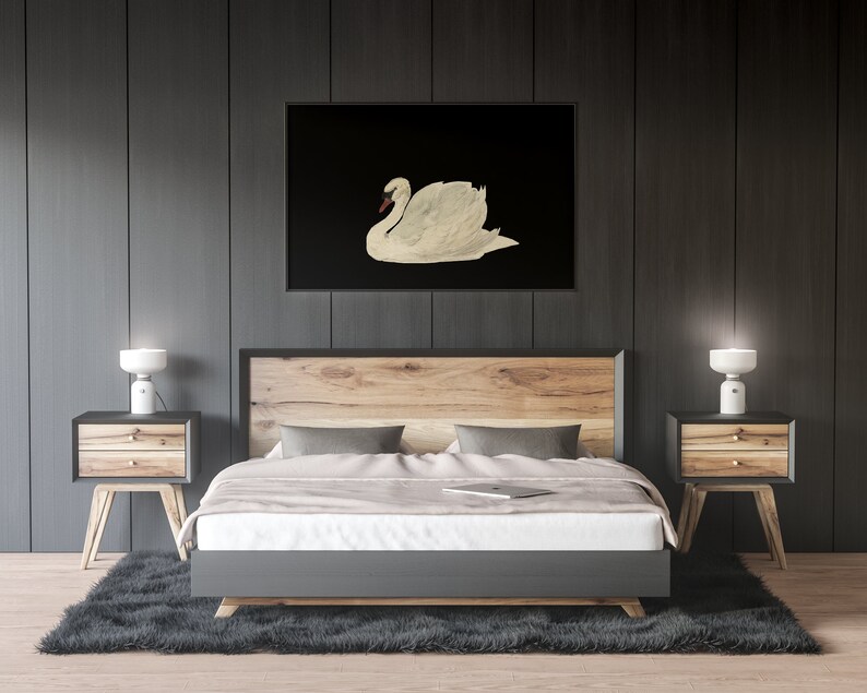 K&ouml;nnte beinhalten: Ein Schlafzimmer-Interieur mit einem Bett, zwei Nachttischen und Lampen. Das Bett hat ein h&ouml;lzernes Kopfteil und ein graues Fu&szlig;teil. Die Nachttische sind aus Holz und haben zwei Schubladen. Die Lampen sind wei&szlig; und haben ein schlichtes Design. Ein schwarz-wei&szlig;es gerahmtes Bild eines wei&szlig;en Schwans h&auml;ngt an der Wand &uuml;ber dem Bett.