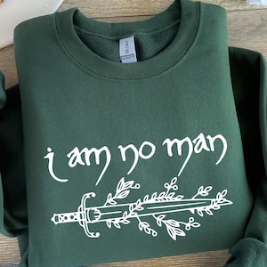 May include: A dark green sweatshirt with a white design of a sword with leaves and the text "i am no man".