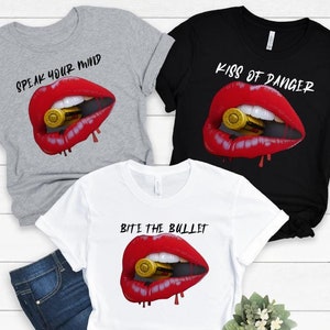 May include: Three t-shirts with different slogans and a red lip design with a bullet in the mouth. The slogans are "Speak Your Mind", "Kiss of Danger", and "Bite the Bullet".