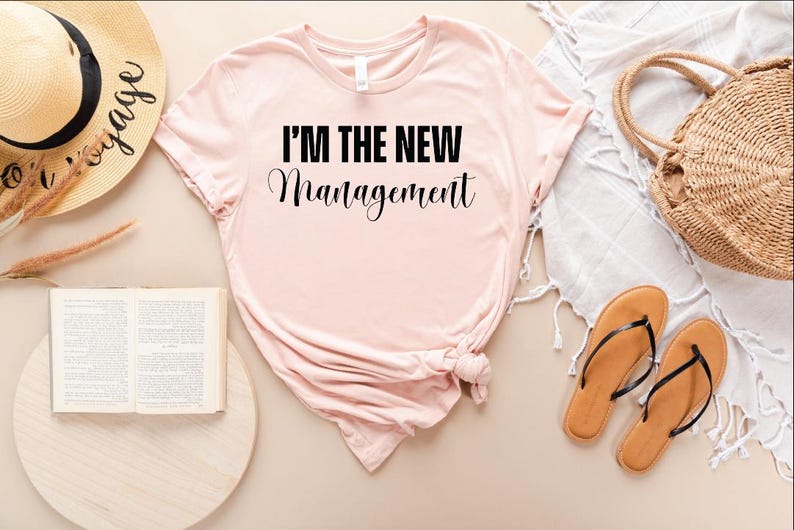 Pu&ograve; includere: Una maglietta rosa con il testo "I'm the new management" in lettere nere.