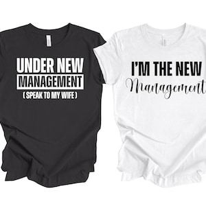 Pu&ograve; includere: Due t-shirt bianche e nere con un messaggio divertente per una coppia. La maglietta nera dice "Sotto nuova direzione (Parla con mia moglie)". La maglietta bianca dice "Sono la nuova direzione".