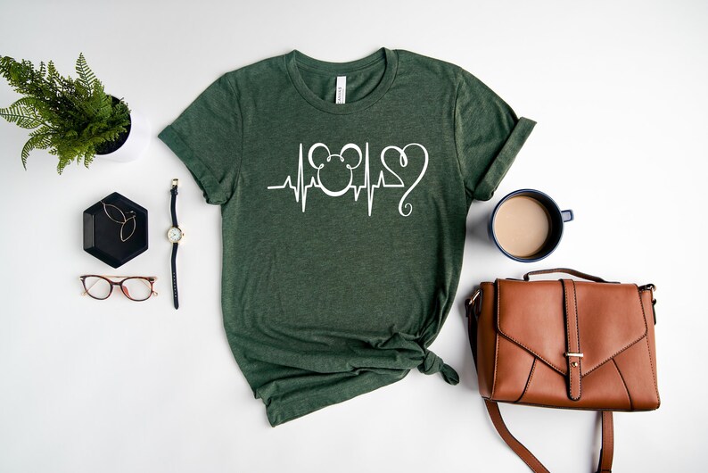 Op de afbeelding: Een groen T-shirt met een witte afbeelding van een hartslag met een Mickey Mouse-hoofd en een hart.