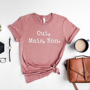 May include: A dusty rose colored t-shirt with the text "Oui, Mais, Non." printed in white.