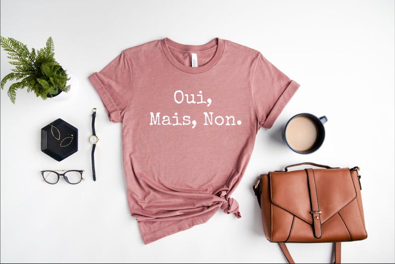 May include: A dusty rose colored t-shirt with the text "Oui, Mais, Non." printed in white.