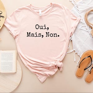 May include: A pink t-shirt with the text "Oui, Mais, Non." printed in black.