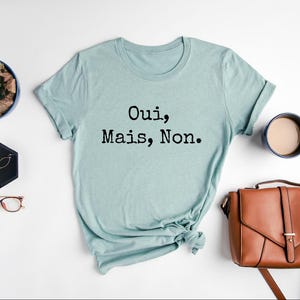 May include: A light blue t-shirt with the text "Oui, Mais, Non." printed in black.