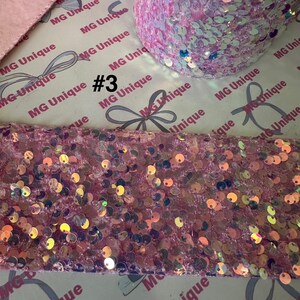 Op de afbeelding: Roze paillettenlint en stof met iriserende pailletten. De afbeelding toont een rol lint en een stuk stof, beide bedekt met glinsterende pailletten. De tekst "#3" is zichtbaar op de achtergrond.