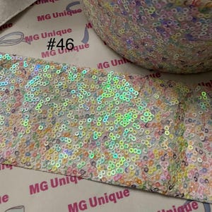 May include: A roll of iridescent sequin trim in pastel colors, including pink, yellow, and blue. The trim is on a white background with the text "MG Unique" and the number "46".